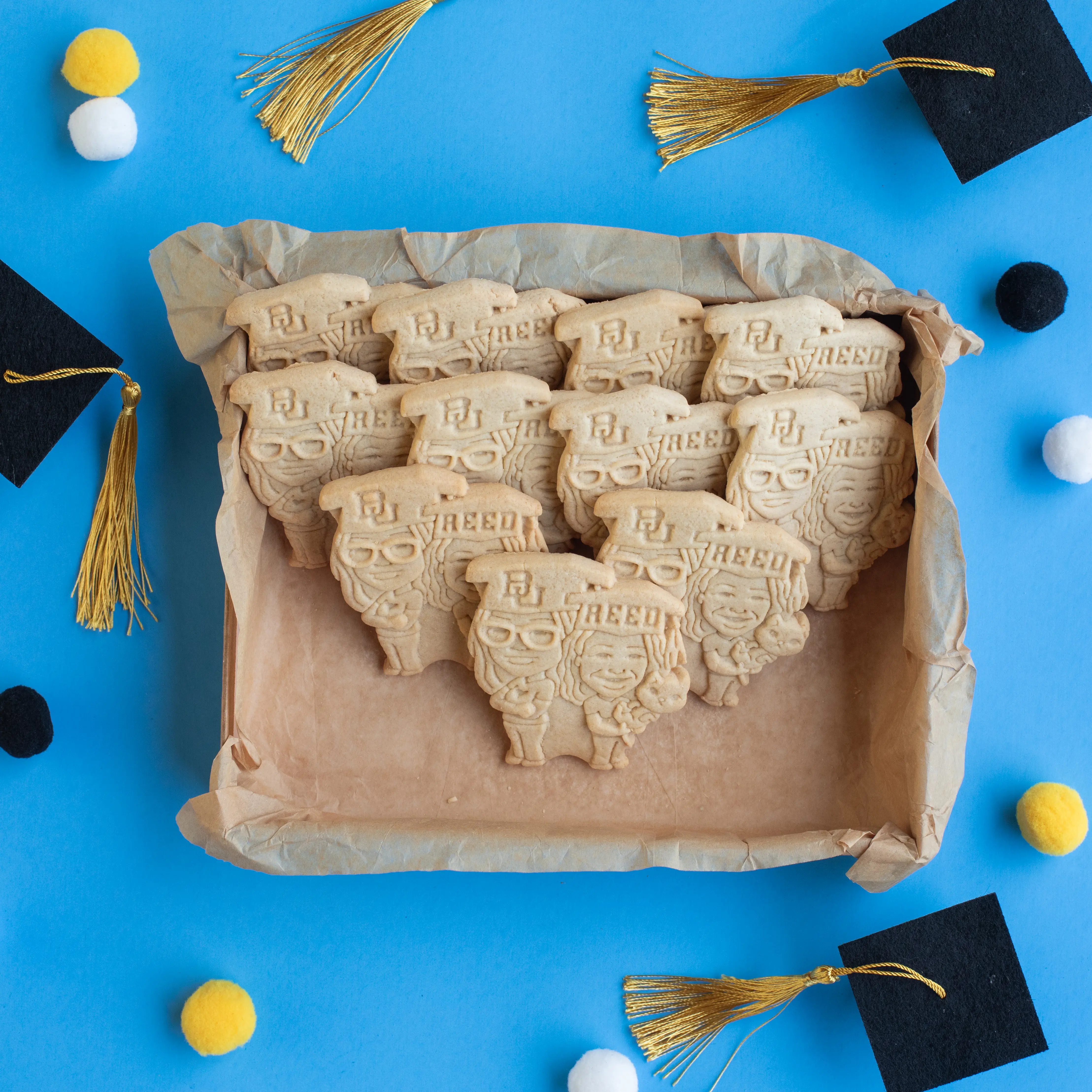 Box of custom graduation face cookies with mini graduation cap decorations